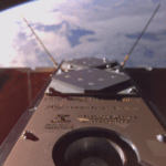 The first image taken by the SpIRIT selfie camera, acquired over New Zealand at the end of the thermal radiator deployment sequence. The camera captures the underside of SpIRIT satellite, where mission participant logos are printed. The image includes the electric propulsion thruster payload of SpIRIT (cylindrical aperture near the bottom) and telecommunication transceivers (diamond patches and antennae). The backs of the solar panels are also visible.